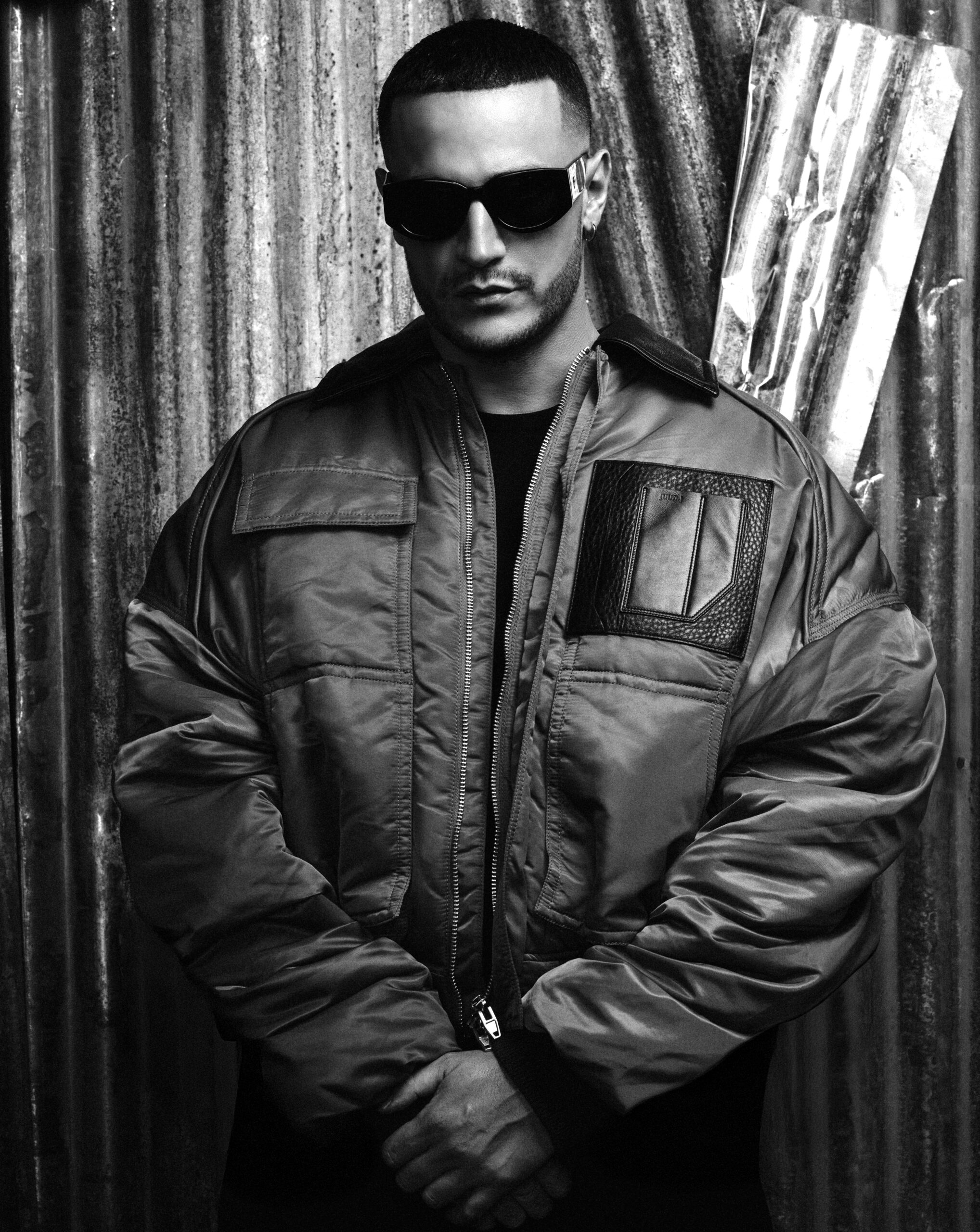 En concert à Paris le 10 mai 2025, l'artiste Dj Snake prend la pose dos à un mur en fer, dans un cliché en noir et blanc.